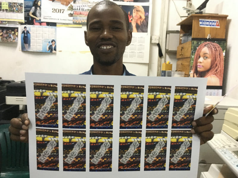 Onesmo in Tanzania proudly showing us our brand new printed Kitenge swing tickets at his print shop before cutting begins