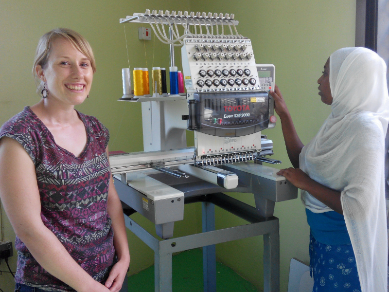 Sian and Asia standing next to the computerised embroidery machine which makes all of Kitenge Store's brand and size labels