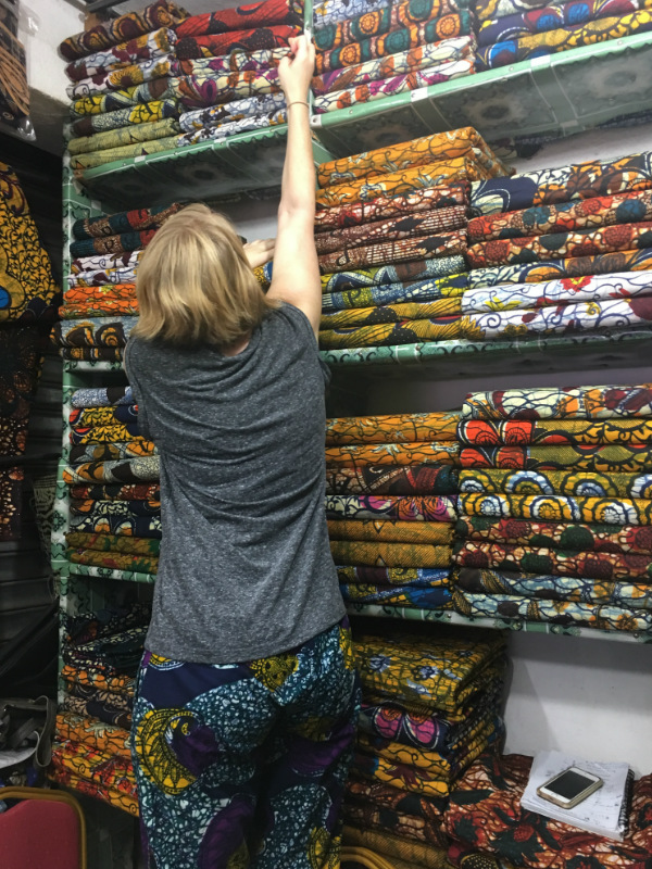 Kitenge founder Sian standing on a chair at the market in Tanzania trying to reach the best African wax print fabrics to make our modern afrocentric clothing