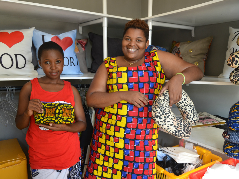 Kitenge-accessories-tailor-Betty-with-her-manager-upendo-standing-inside-her-shop-in-Tanzania-with-some-of-their-handmade-African-print-cushions
