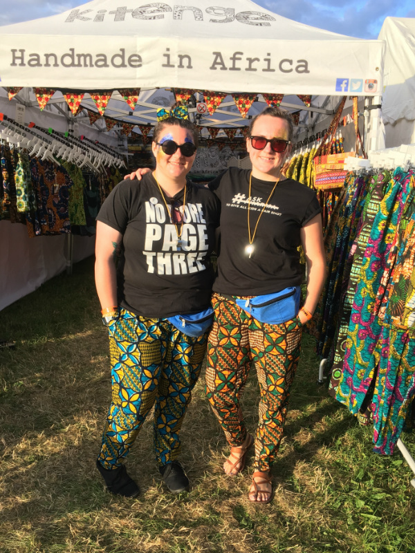 Kitenge volunteers Emily and Dawn standing outside our stall at WOMAD Festival modelling our colourful African print trousers