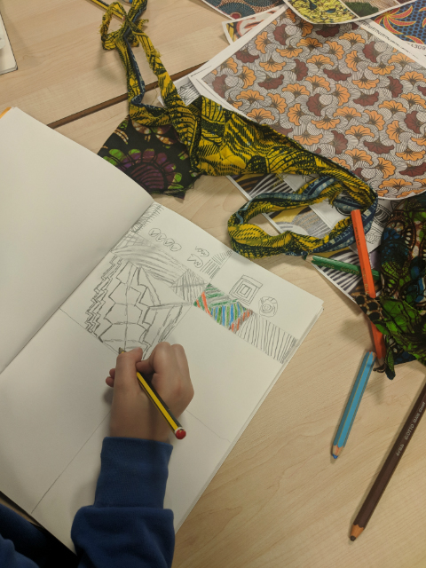 Child sketching African print clothing fabrics in school art class