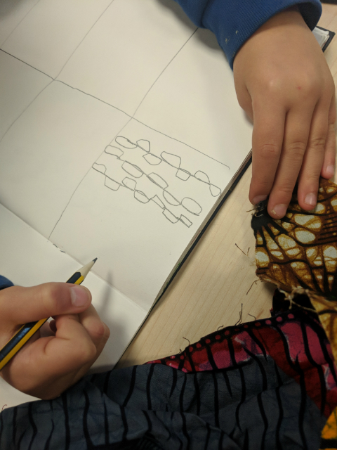 Year 2 pupil drawing with pencil a traditional African clothing fabric pattern in their sketchbook during an art class