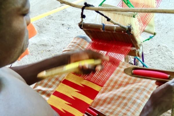 Kente weaver Ghana using shuttle pass weft through warp handloom
