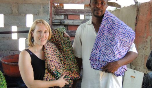 Kitenge Store Founder Sian visited Daniel at his batik making workshop in Ghana West Africa holding two different finished colourful fabric designs used to make modern afrocentric clothing