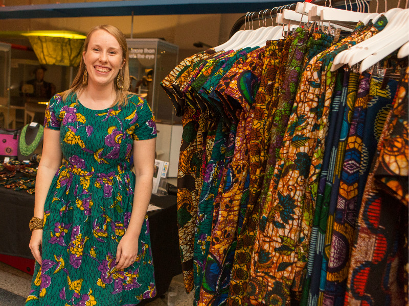 Kitenge Store founder Sian standing in front of the stall and rail of colourful African print clothing at the Fabric Africa fashion show organised by Bristol Museum