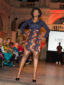 A female model wearing a red African print skirt in a pencil style and a black African beaded necklace to match at the Fabric Africa Fashion Show in Bristol Museum UK