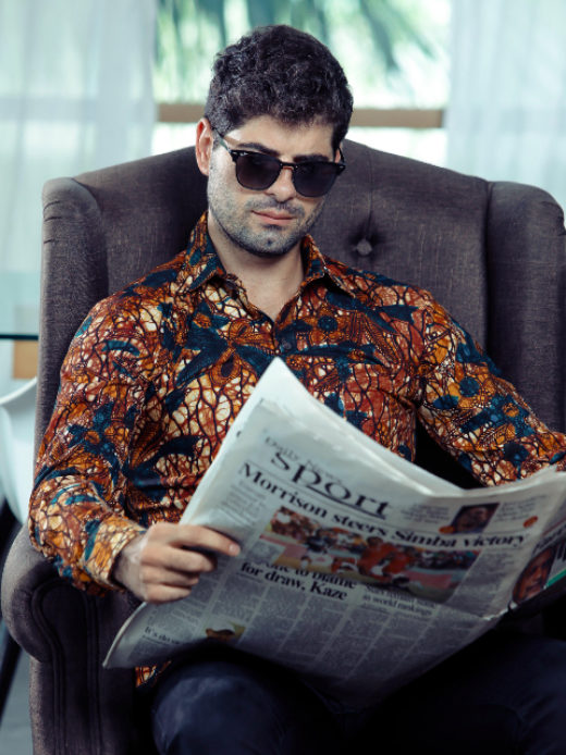 Men's gold floral custom-made African print long sleeve shirt model wearing sat in arm chair reading newspaper