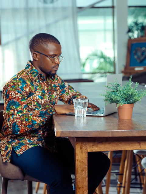 Men's green floral custom-made African print long sleeve shirt model wearing sat down working on laptop side view