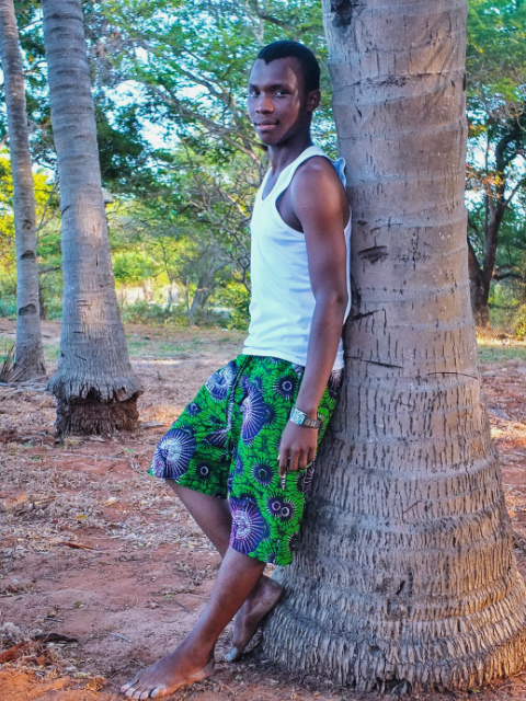 African menswear model wearing green African print shorts on the beach in Tanzania