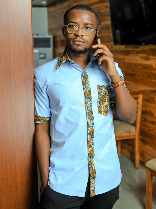 Men's custom-made plain light blue short sleeve shirt with optional ankara fabric contrasts model wearing front view using phone