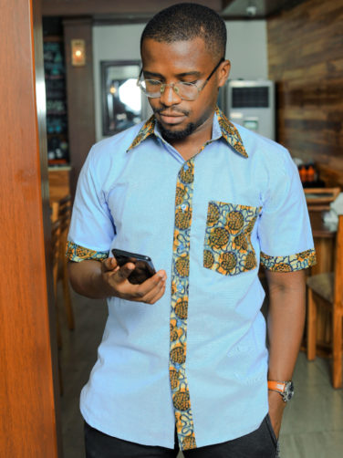 Men's custom-made plain light blue short sleeve shirt with optional ankara fabric contrasts model wearing looking at phone
