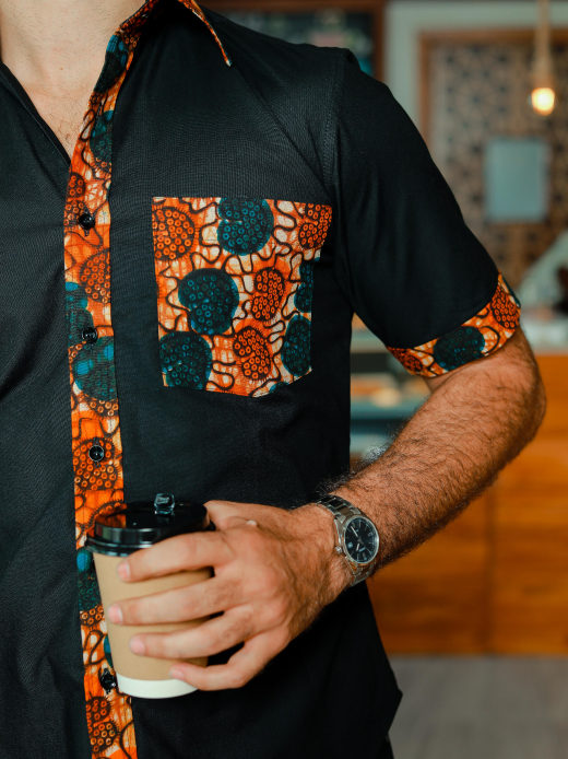Men's plain black short sleeve shirt with optional African print fabric contrasts model wearing pocket and button placket closeup
