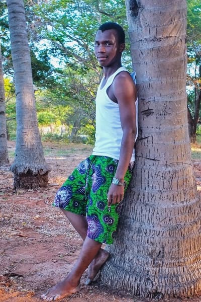 Male model wearing African print fabric made to measure shorts by Kitenge Store standing next to palm tree