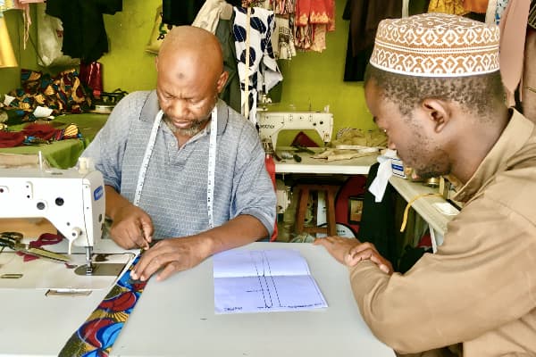 Kitenge master tailor teaching apprentice how to make African necktie Tanzania
