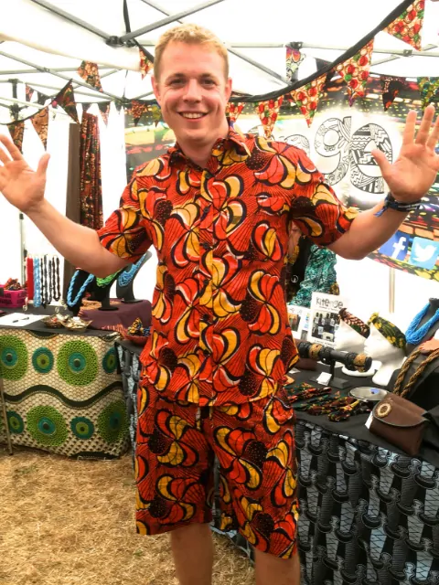 Men's red yellow African print short sleeve shirt and matching shorts kitenge customer wearing at Womad world music festival UK